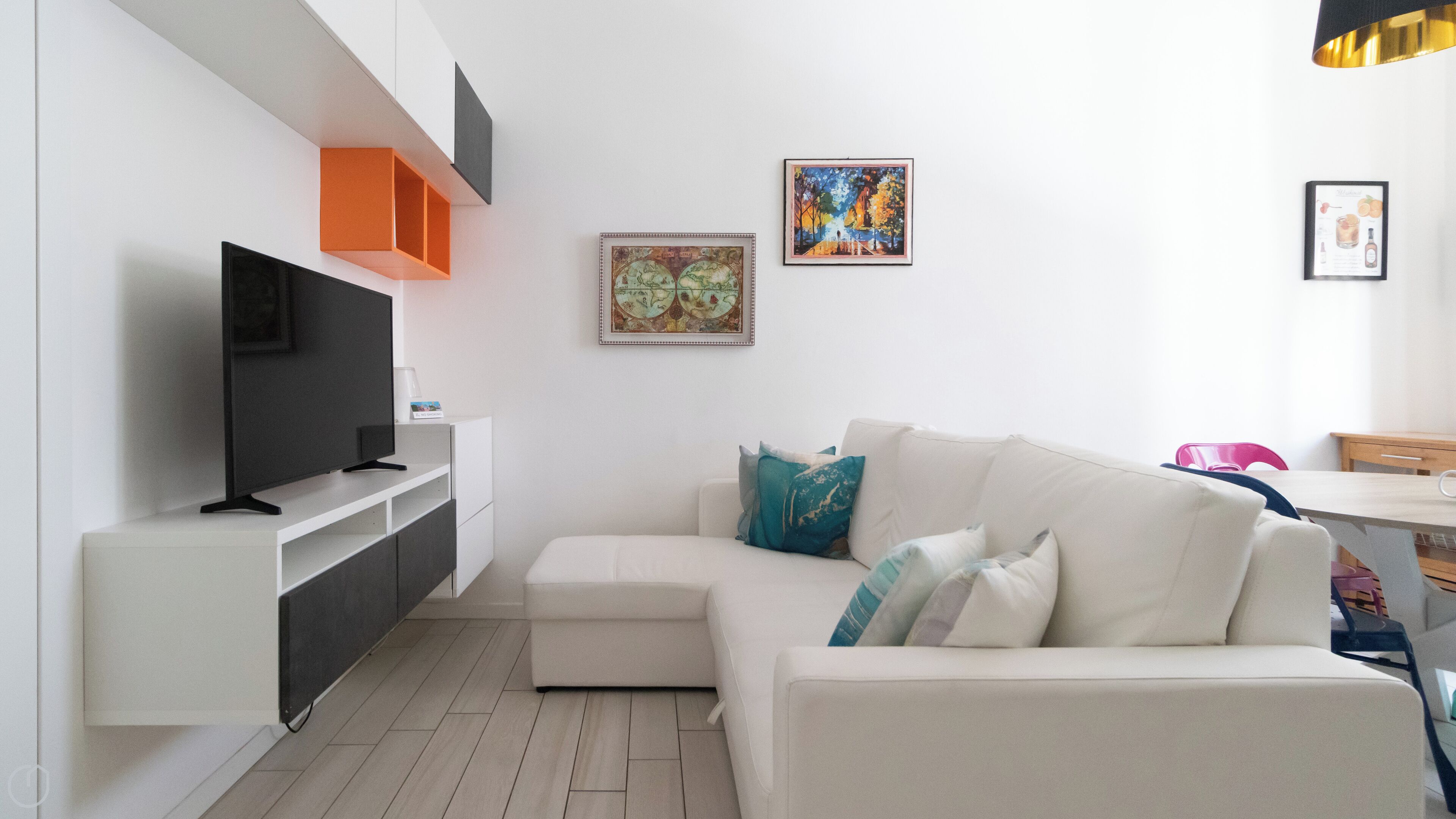 A modern living room with a flat-screen TV, white sofa, and orange shelving unit.