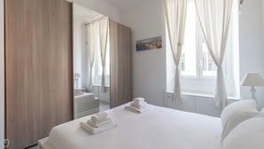 A hotel room with a bed, a mirror, a window with curtains, a bedside table, and a lamp. - Italianway Easy - Arbe 51 (Milan)