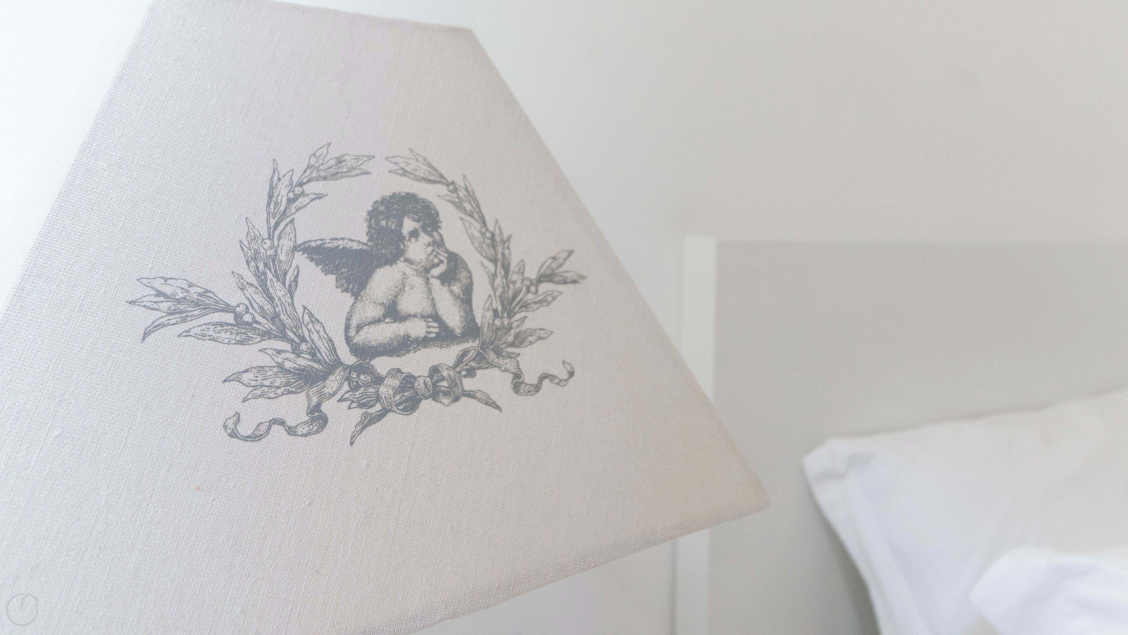 Een lamp met een decoratief ontwerp op de kap, een wit kussen, en een effen muur op de achtergrond.