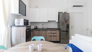 A modern kitchen with white cabinets, a stainless steel refrigerator, a microwave, and a sink. There is a wooden dining table with two white mugs. - Italianway Easy - Arbe 51 (Milan)