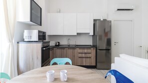 A modern kitchen with white cabinets, a stainless steel refrigerator, and a microwave. There is a wooden table with two white mugs. - Italianway Easy - Arbe 51 (Milan)