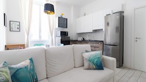 A modern apartment with a white sofa, teal cushions, a kitchen with white cabinets, a stainless steel refrigerator, and a flat-screen TV mounted on the wall. - Italianway Easy - Arbe 51 (Milan)
