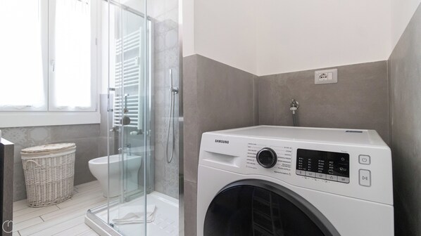 Un baño moderno con cabina de ducha de vidrio, lavadora blanca y una cesta de mimbre.