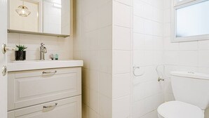 A bathroom with a white toilet, a sink with a mirror above it, and a cabinet with drawers. - Central 1BR in Dizzengoff by Holiday-rentals (Tel Aviv-Yafo)