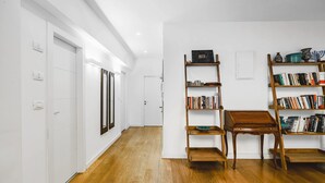 Un couloir doté d’un plancher en bois, de murs blancs et d’une bibliothèque contenant des livres et des objets décoratifs.