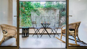 Une terrasse dotée de meubles en osier, d’une table et de chaises, donnant sur un jardin agrémenté d’une clôture en métal et de verdure.