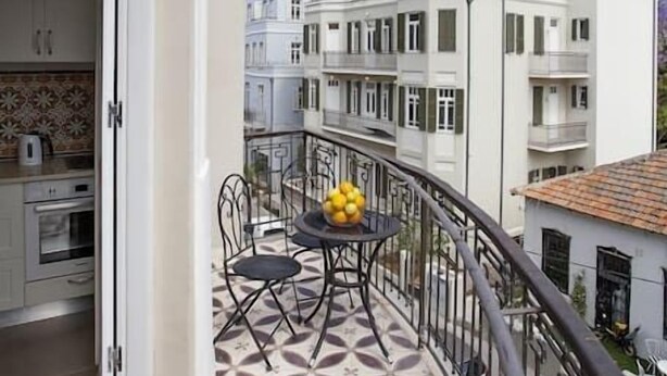 Een balkon met een patroon in de vloer, een tafel met stoelen en uitzicht op omliggende gebouwen.