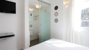 Een moderne hotelkamer met een bed, een aan de muur bevestigde televisie, een glazen schuifdeur naar een badkamer en drie decoratieve wandplaten.