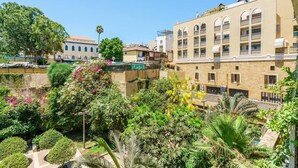 Um pátio com vegetação exuberante, piscina e um edifício com várias varandas.
