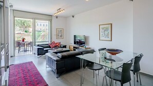 Uma sala de estar moderna com uma mesa de jantar de vidro, sofá de couro preto e uma televisão.