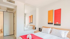 Quarto de hotel com uma cama grande, um espelho, duas paredes em vermelho e uma porta para o banheiro.