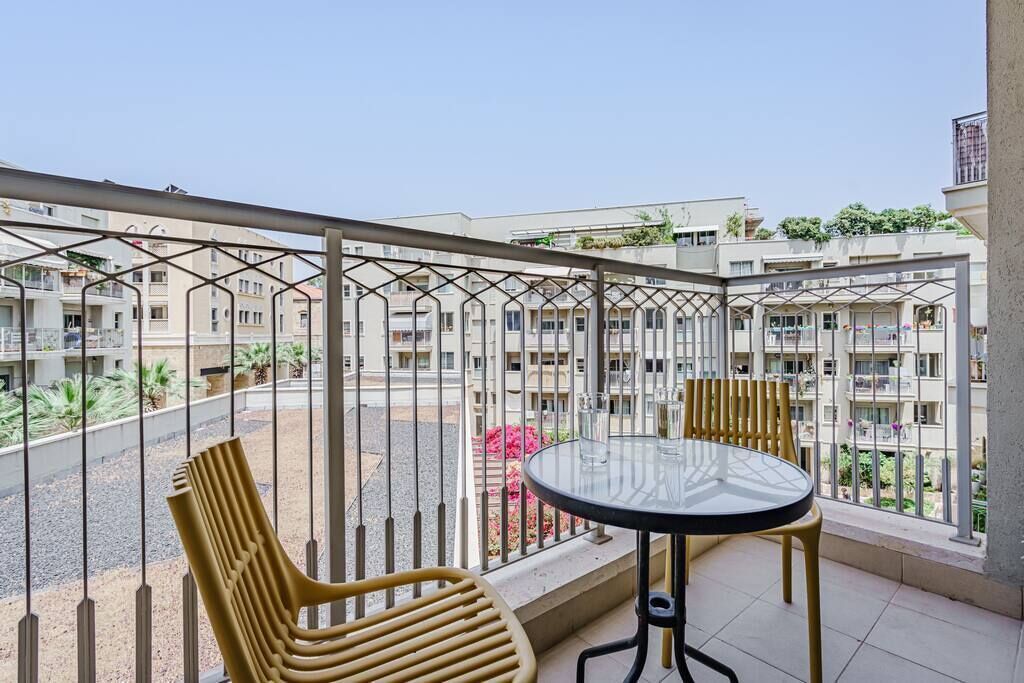 Un balcon avec une table ronde et deux chaises, donnant sur un quartier résidentiel composé de plusieurs immeubles.