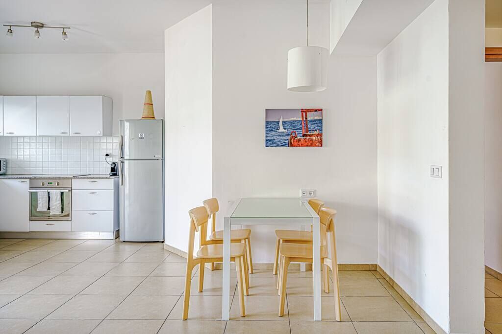 A modern kitchen with white cabinets, a glass dining table, and wooden chairs.