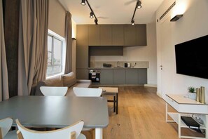 A modern living space with a dining area, kitchen, and a large TV screen.