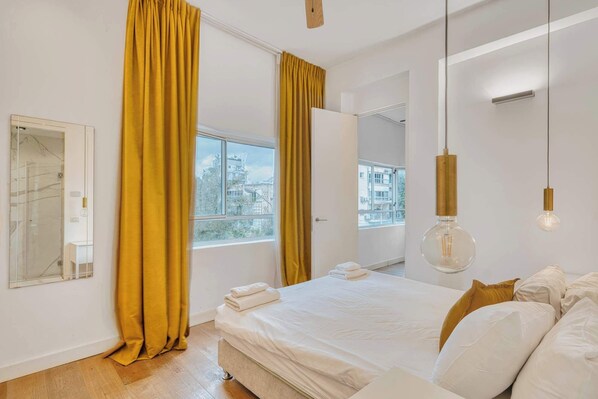 A modern bedroom with a large bed, a view of the city, and a mirror.