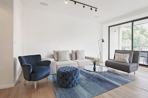 A modern living room with a sofa, two armchairs, a round coffee table, and a blue ottoman.