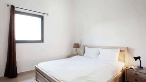 A bedroom with a bed, bedside table, lamp, and a window with curtains. - Cute Shenkin area 1BR By Holiday-rentals SAFE ROOM ({{addressCityy}})