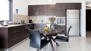 A modern kitchen with dark wood cabinets, a stainless steel refrigerator, and a dining table with four chairs. - Cute Shenkin area 1BR By Holiday-rentals SAFE ROOM ({{addressCityy}})