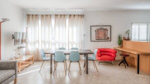 Ein modernes Wohnzimmer mit Essbereich, einem roten Sessel, einem Fernseher und einem gerahmten Bild an der Wand.