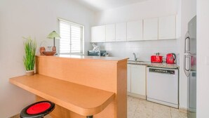 Eine moderne Küche mit weißen Schränken, einer Holz Arbeitsplatte, einem Geschirrspüler und einem roten Wasserkocher.