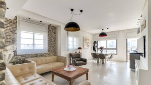 A modern living room with a stone accent wall, leather sofas, a wooden coffee table, and a dining area with a white table and chairs. - Wonderfull duplex 3BR Hakovshim SAFE ROOM ({{addressCityy}})