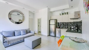 Eine moderne Wohnung mit Wohnzimmer, das eine Sitzecke mit Sofa und Hocker sowie eine Küche mit Kühlschrank und gefliestem Spritzschutz und einem wandmontierten Spiegel bietet.