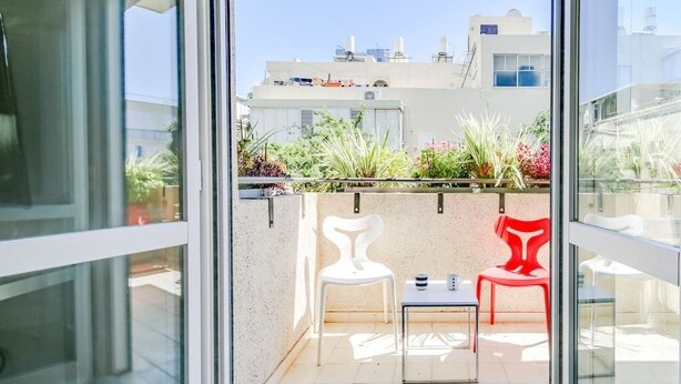 Ein Balkon mit zwei Stühlen, einem weißen und einem roten, und einem kleinen Tisch.