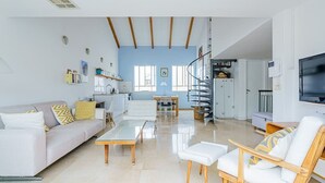 A spacious living room with a sofa, coffee table, and chairs, a kitchen area with a dining table, and a spiral staircase.