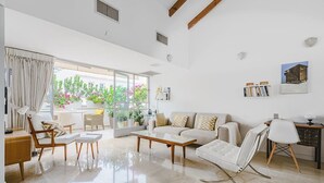 A spacious living room with a sofa, coffee table, and chairs, a dining area with a table and chairs, and a balcony with plants.