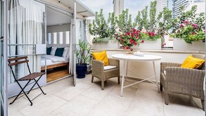 A balcony with a bed, wicker chairs, a round table, and potted plants.