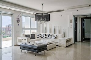 Una sala de estar moderna con un ventanal grande, una araña, un conjunto de sofás y una mesa de centro.