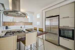 A modern kitchen with a gas stove, stainless steel appliances, and a central island with bar stools. - Duplex Penthouse 3BR Asirey Tsion SAFE ROOM ({{addressCityy}})