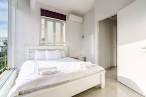 A modern bedroom with a large bed, a window with a view, and an air conditioning unit.