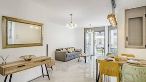 Una sala de estar moderna con un sofá, una mesa de comedor y sillas. Hay un espejo grande en la pared y un aparador con cajones.