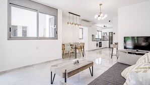 Una sala de estar moderna con un ventanal grande, una zona de comedor y una cocina al fondo.