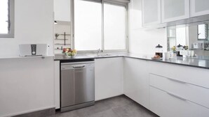 A modern kitchen with white cabinetry, a dishwasher, and a window with blinds. - Central 3BR in Rupin by Holiday-rentals SAFE ROOM ({{addressCityy}})