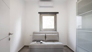 A small, modern room with a grey sofa, a window with blinds, and a door. - Central 3BR in Rupin by Holiday-rentals SAFE ROOM ({{addressCityy}})