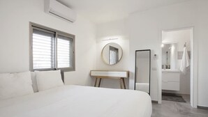 A modern bedroom with a large bed, a bedside table, a mirror, and a view into a bathroom. - Central 3BR in Rupin by Holiday-rentals SAFE ROOM ({{addressCityy}})
