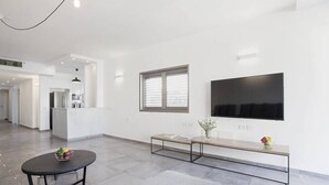 A spacious living area with a modern kitchen in the background, a large flat-screen TV mounted on the wall, and a bench with a vase of flowers. - Central 3BR in Rupin by Holiday-rentals SAFE ROOM ({{addressCityy}})