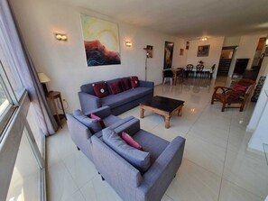 A modern living room with a grey sofa set, a coffee table, and a dining area with chairs and a table.