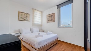 A bedroom with a bed, a nightstand, a dresser, a window with a view, and two framed pictures on the wall. - Spacious 2BR  Ha-Medina Square SAFE ROOM (Tel Aviv-Yafo)
