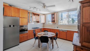 A modern kitchen with wooden cabinets, a stainless steel refrigerator, a dining table with chairs, and a ceiling fan. - Spacious 2BR  Ha-Medina Square SAFE ROOM (Tel Aviv-Yafo)