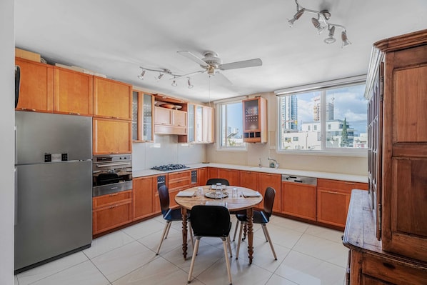 A modern kitchen with wooden cabinets, a stainless steel refrigerator, a dining table with chairs, and a ceiling fan.