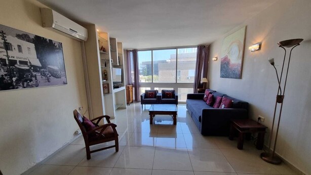 A spacious living room with a sofa, armchair, and coffee table. There is a large window providing natural light and a view of the outside. - Spacious 2BR  Ha-Medina Square SAFE ROOM (Tel Aviv-Yafo)