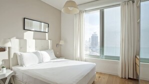 Une chambre d’hôtel moderne dotée d’un grand lit, offrant une vue sur la ville, et présentant un design minimaliste.