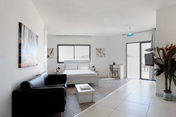 Une chambre d’hôtel moderne avec un lit, un canapé en cuir noir, une petite table blanche, un bureau et un téléviseur.