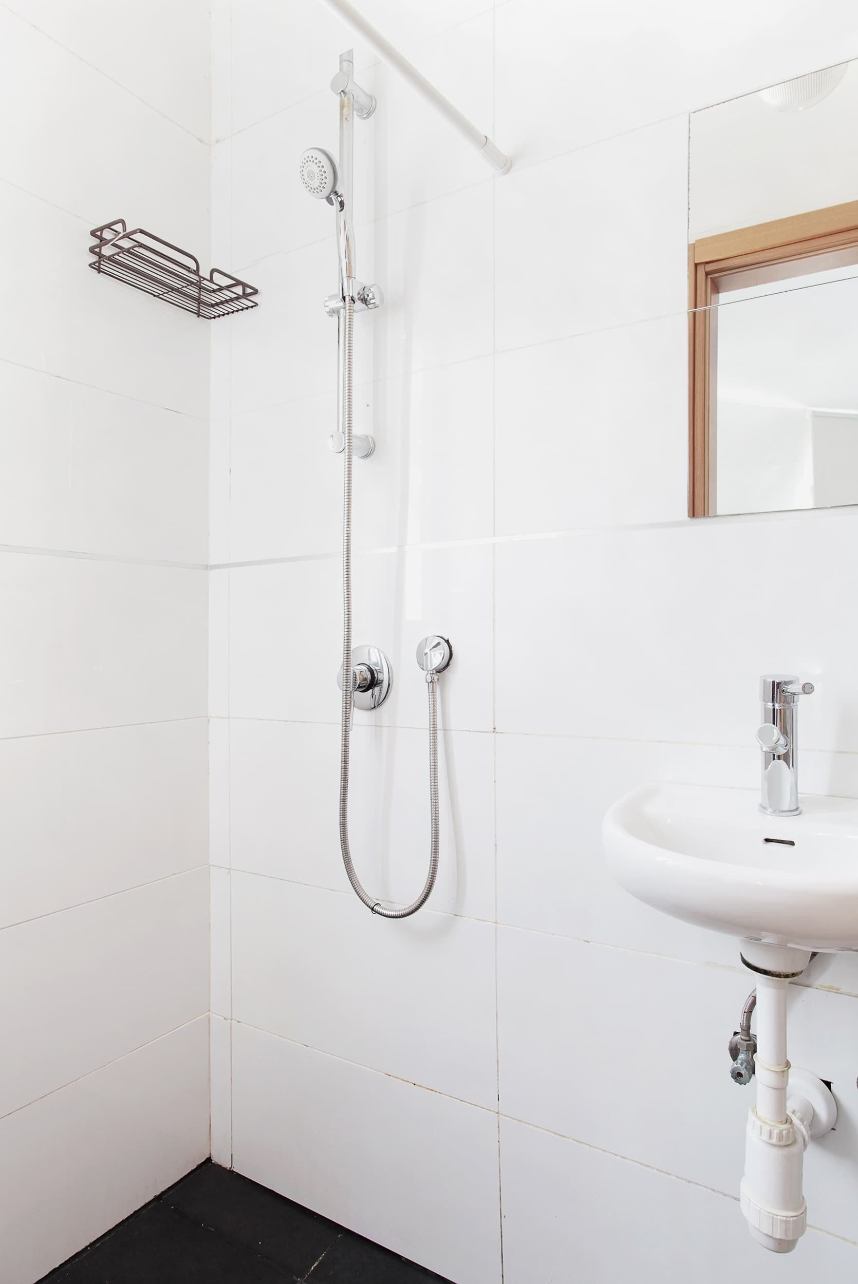 Une salle de bain avec des murs carrelés de blanc, une douche avec un pommeau flexible, un lavabo avec un miroir et un porte-serviettes.