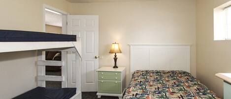 A room with bunk beds, a nightstand with a lamp, and a bed with a patterned bedspread.