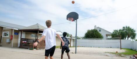 En basketballbane med kurv, hegn og huse i baggrunden.