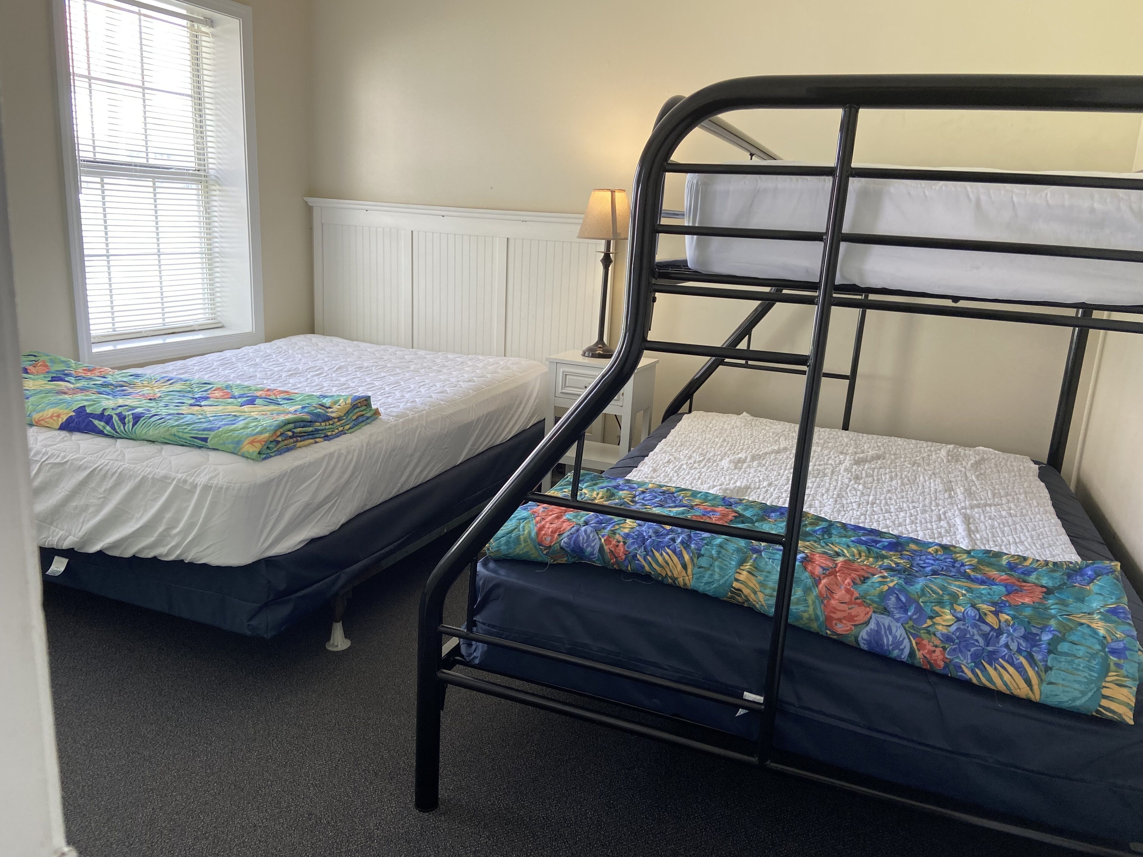 Une chambre de dortoir avec deux lits superposés, chacun recouvert d’une courtepointe à motifs floraux colorés.